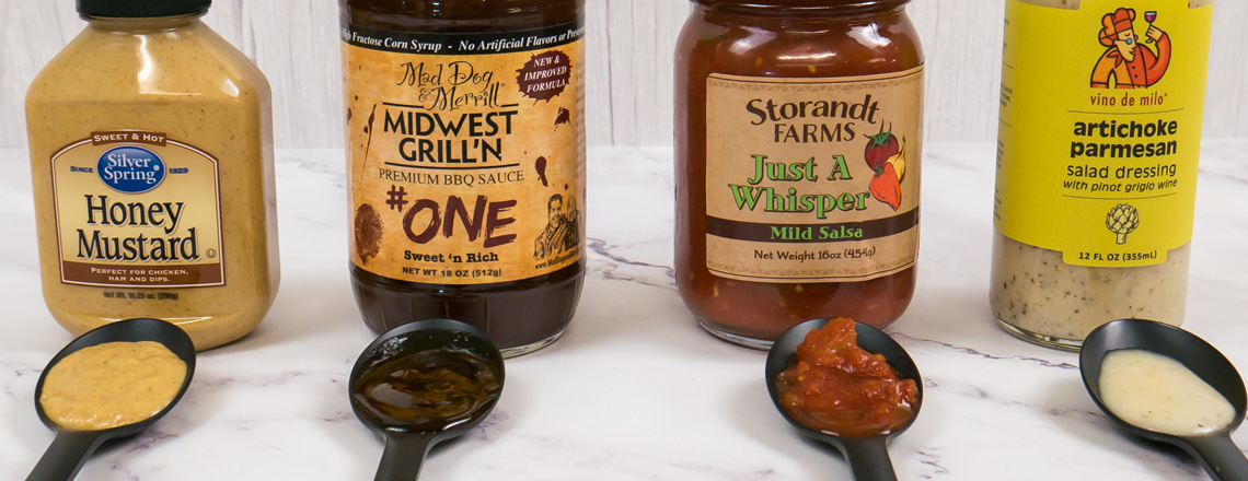 Assortment of condiments - Silver Spring Honey Mustard, Mad Dog & Merrill BBQ Sauce, Storandt Farms Salsa, and Vino de Milo Salad Dressing - all available for purchase online and at the Westby Cooperative Creamery Retail Store.