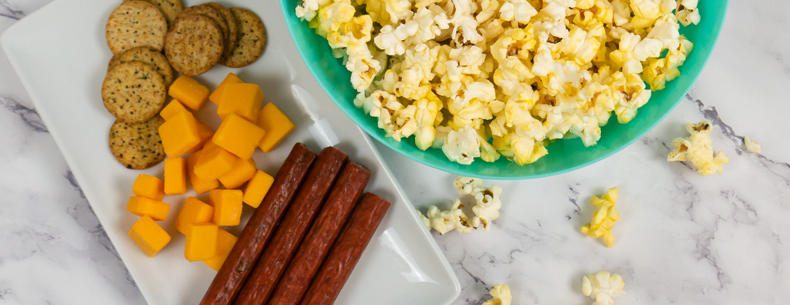 Wisconsin made crackers, cheese, and meat sticks next to a bowl of popcorn - all available for purchase online and at the Westby Cooperative Creamery Retail Store.