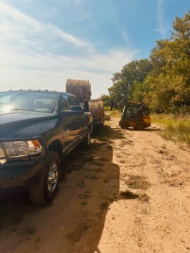 A pick up truck with a trailer of hay.