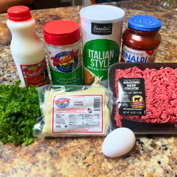 Ingredients needed to put together String Cheese-Stuffed Meatballs - milk, Westby grated parmesan, Westby string cheese, parsley, ground beef, pasta sauce, breadcrumbs, and an egg.