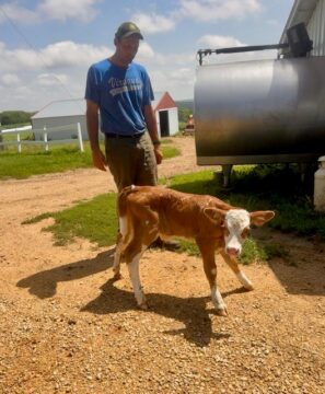 Farmer-owner Drew Rogers standing next to a newborn Jersey calf outside of the barn.